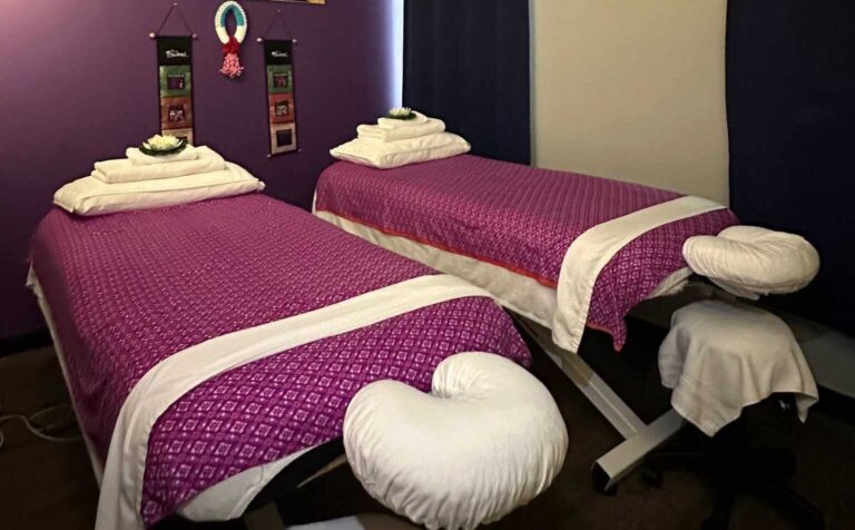 Two side-by-side massage tables with purple covers and folded white towels at Siam Thai Yoga Massage
