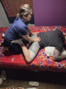 A therapist supporting a bent leg during clothed Thai massage on a treatment table