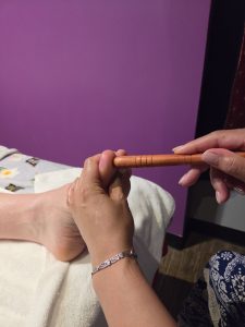 A therapist supporting a foot while using a wooden tool during Thai reflexology